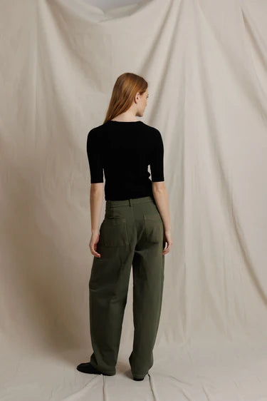Person wearing a black top and green pants against a beige backdrop