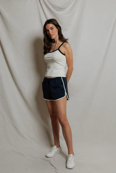 Woman wearing a white tank top and navy shorts against a plain background