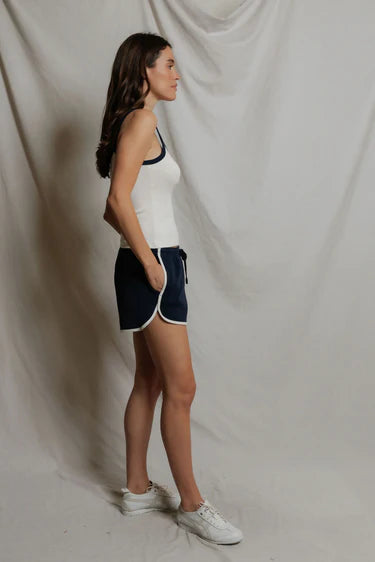 Woman wearing a white tank top and navy shorts against a plain background