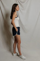 Woman wearing a white tank top and navy shorts against a plain background
