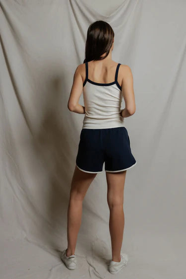 Person wearing a white tank top and navy shorts standing against a plain background