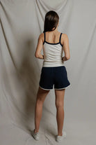 Person wearing a white tank top and navy shorts standing against a plain background