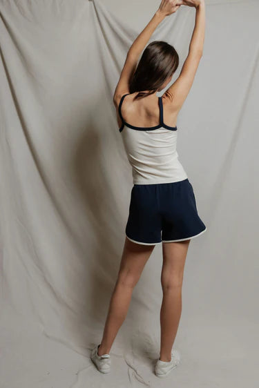 Person wearing a white tank top and navy shorts against a plain background