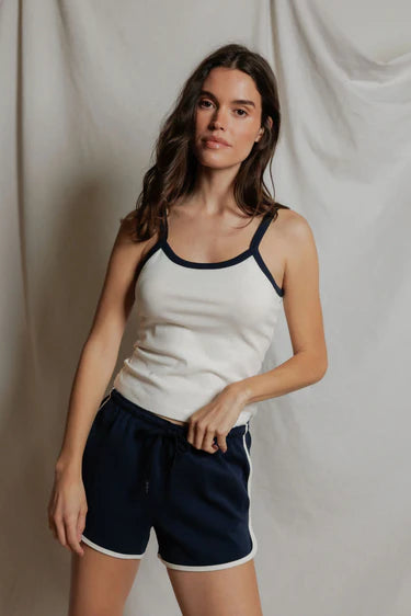 Woman wearing a white tank top with navy trim and navy shorts against a plain background