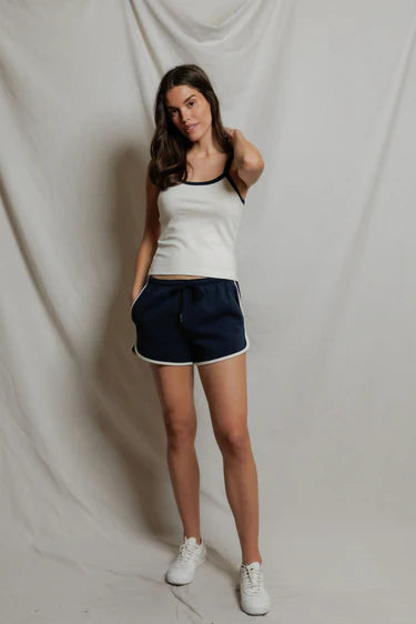 Woman wearing a white tank top and navy shorts against a plain background
