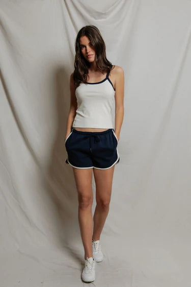 Woman wearing a white tank top and navy shorts against a plain background