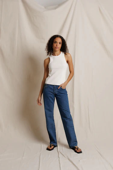 Woman wearing a white sleeveless top and blue jeans against a plain background