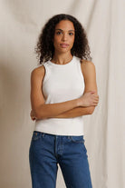 Woman wearing a white sleeveless top and blue jeans against a beige background