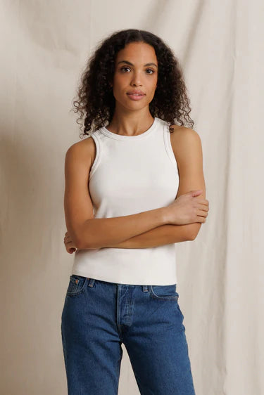 Woman wearing a white sleeveless top and blue jeans against a beige background