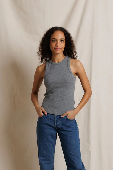 Woman wearing a gray tank top and blue jeans against a beige background