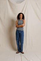 Woman wearing a gray tank top and blue jeans standing against a plain background