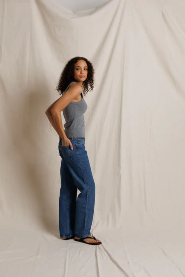 Woman wearing a gray tank top and blue jeans standing against a plain white background