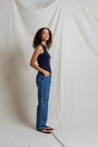 Woman wearing a navy tank top and blue jeans standing against a plain white background