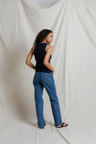 Person wearing a black sleeveless top and blue jeans against a white backdrop