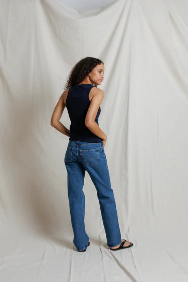 Person wearing a black sleeveless top and blue jeans against a white backdrop