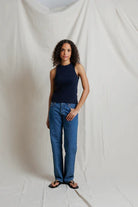 Woman wearing a navy tank top and blue jeans standing against a plain white background
