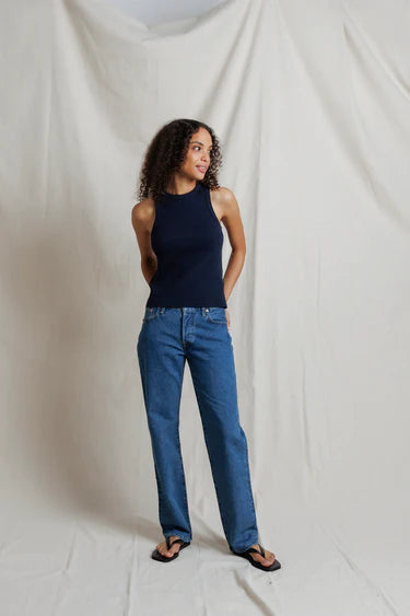 Woman wearing a navy top and blue jeans against a plain white background