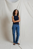 Woman wearing a navy top and blue jeans standing against a plain white background