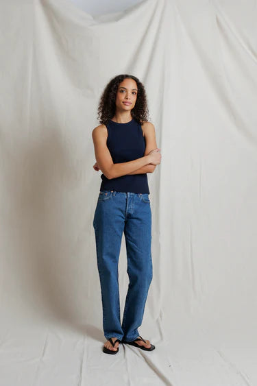 Woman wearing a navy top and blue jeans standing against a plain white background