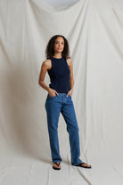 Woman wearing a navy tank top and blue jeans standing against a plain white background