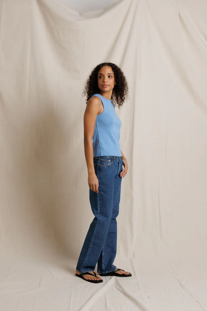 Woman wearing a blue sleeveless top and jeans standing against a plain background