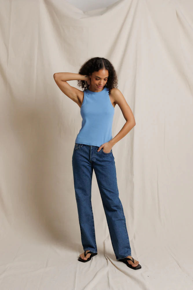 Woman wearing a blue sleeveless top and jeans against a plain background
