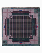 A square collectible gaming mat featuring a detailed board layout for the game Mangolo Ngo. The mat has a dark teal center with a plaid grid, surrounded by a purple and teal plaid border, and printed with game rules, player names, and the Mangolo Ngo logo.