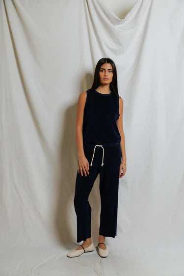 Woman wearing a navy sleeveless top and pants against a white draped curtain background