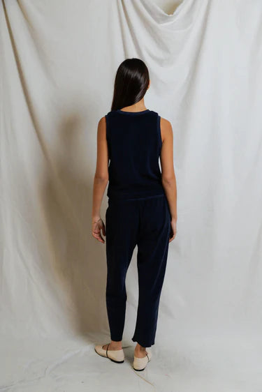 Person wearing a navy blue sleeveless top and pants against a white draped fabric background