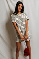 Woman wearing a striped outfit holding a red bag against a plain background
