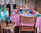 Outdoor dining setup with a pink and white tablecloth, drinks, and cards on a patio.