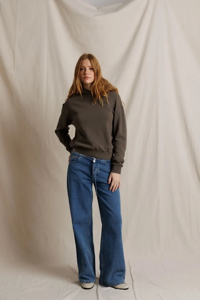 Woman wearing a brown sweater and blue jeans against a plain background