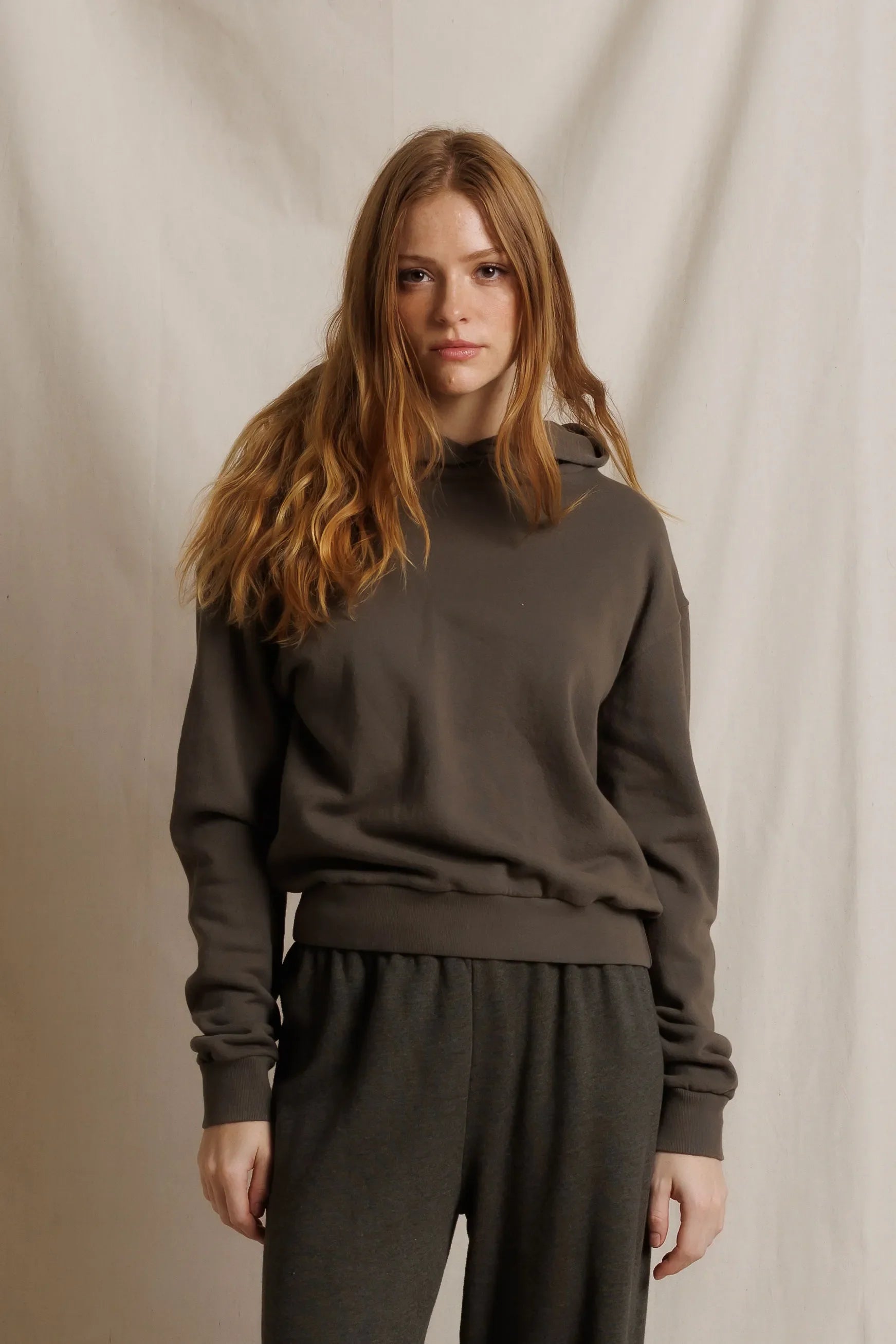 Woman wearing a dark brown sweater and pants against a neutral background