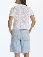 Woman wearing a white lace top and light blue denim shorts on a white background