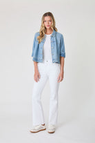 Woman wearing a denim jacket, white t-shirt, and white jeans on a plain background