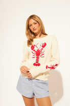Woman wearing a white sweater with red lobster designs on a plain background