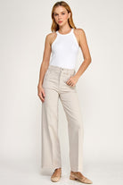 Woman wearing a white sleeveless top and beige pants on a plain background