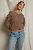 Woman wearing a brown striped sweater and blue jeans against a neutral background