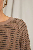 Close-up of a person wearing a brown sweater with black stripes against a neutral background