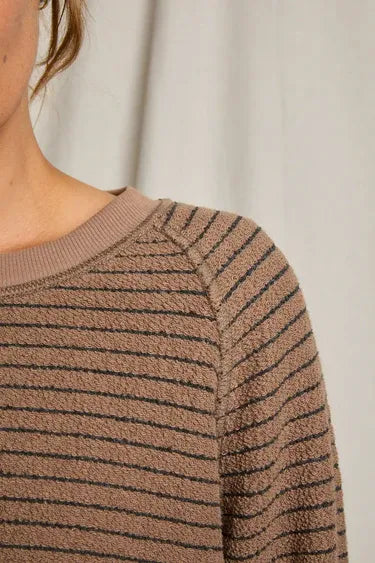 Close-up of a person wearing a brown sweater with black stripes against a neutral background