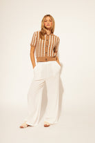 Woman wearing a striped brown and white top with white pants on a beige background