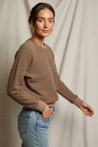 Woman wearing a brown sweater and blue jeans against a plain background