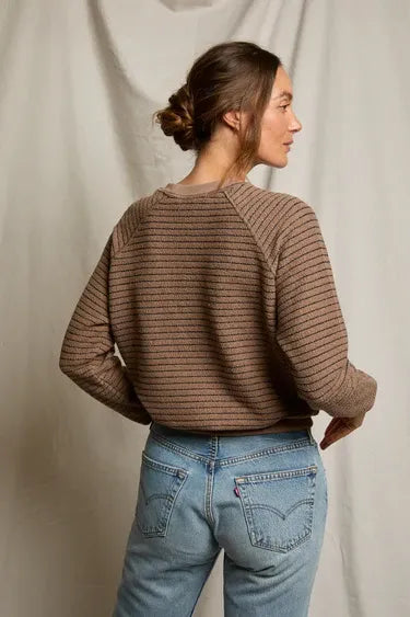 Woman wearing a brown ribbed sweater and blue jeans against a plain background