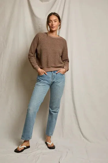 Woman wearing a brown sweater and blue jeans against a plain background