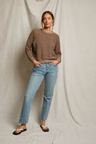 Woman wearing a brown sweater and blue jeans against a plain background