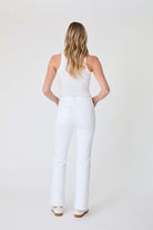 Woman wearing a white sleeveless top and pants on a plain background