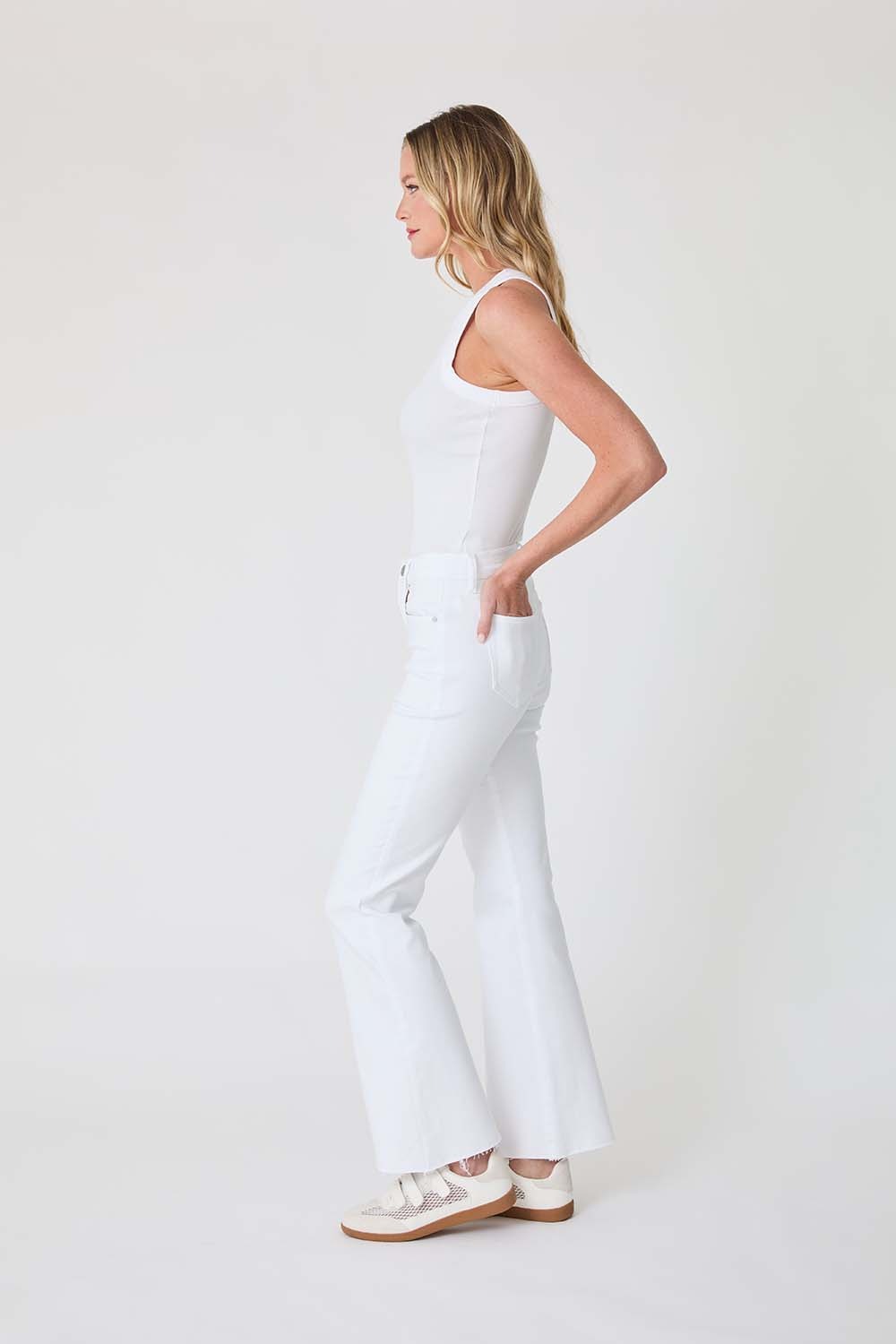 Woman wearing a white sleeveless top and pants on a plain background