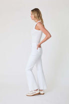Woman wearing a white sleeveless top and pants on a plain background