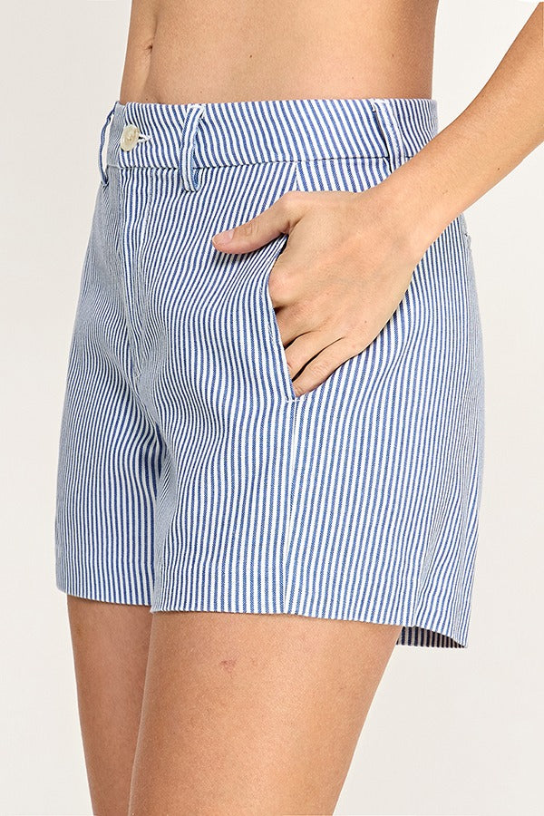 A close-up of a person wearing blue and white vertically striped shorts, with the hand tucked into a side pocket against a plain light background.