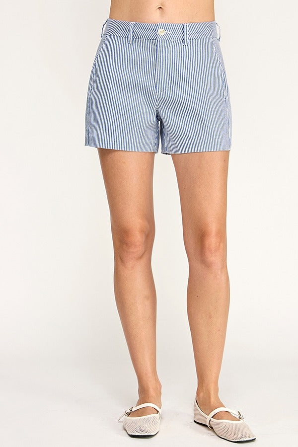 A person wearing light blue and white vertically striped shorts, paired with beige flat shoes, shown from the waist down against a plain light background.